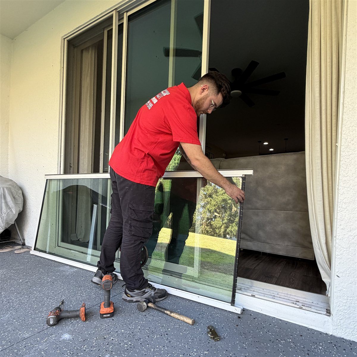 Real Speedy technician in red SPEEDY polo carrying a removed sliding door panel outside a Central Florida home with power drills and hammer staged on the driveway