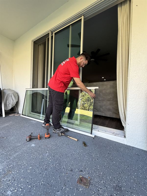 Speedy technician in red SPEEDY polo carrying a removed sliding door panel outside a Central Florida home with two power drills on the ground