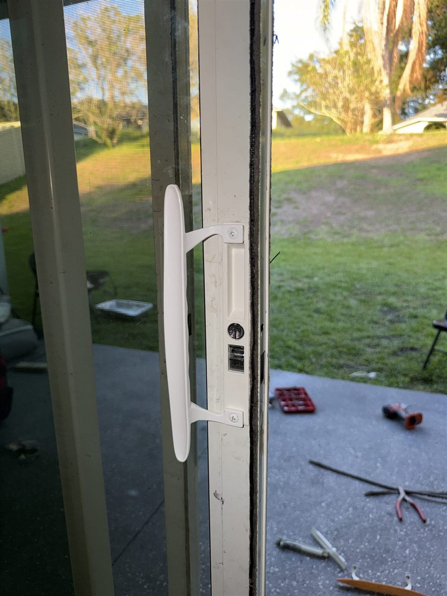 Real Speedy lock system repair in progress: new white sliding door handle installed, mortise lock visible, tools laid out on the patio at a Central Florida home