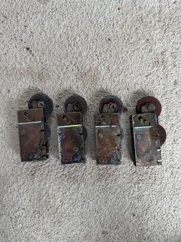 Four worn rusty old sliding door roller assemblies removed from a Central Florida home, lined up before disposal