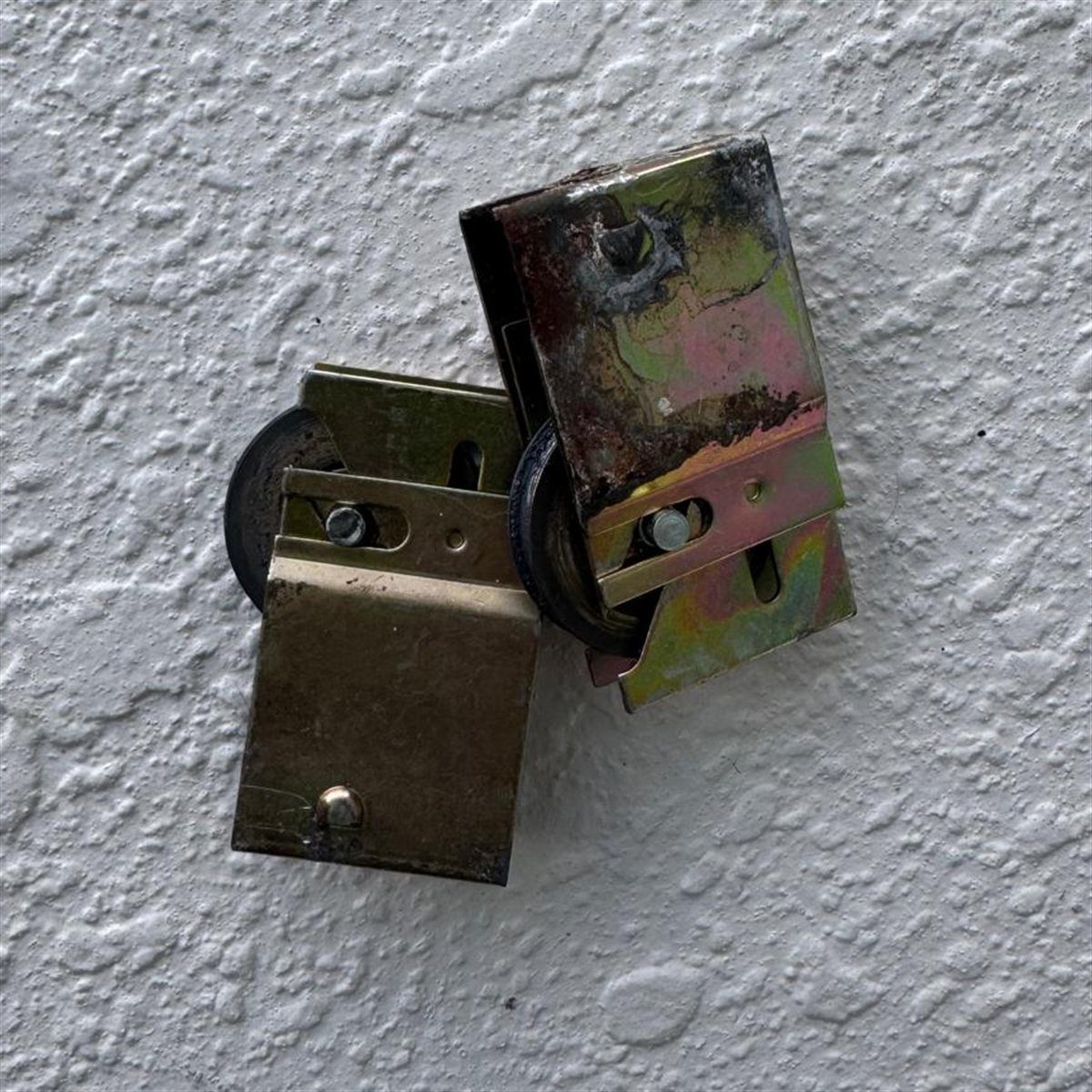 Old corroded sliding door roller assembly next to a brand new brass-finish stainless replacement mounted side by side