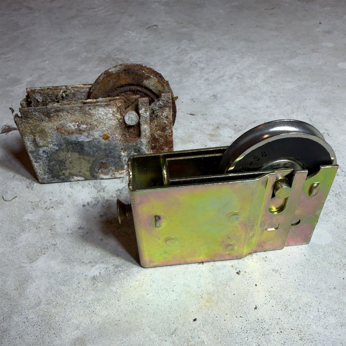 Worn-out old sliding door roller compared to a fresh new stainless steel roller assembly on the floor