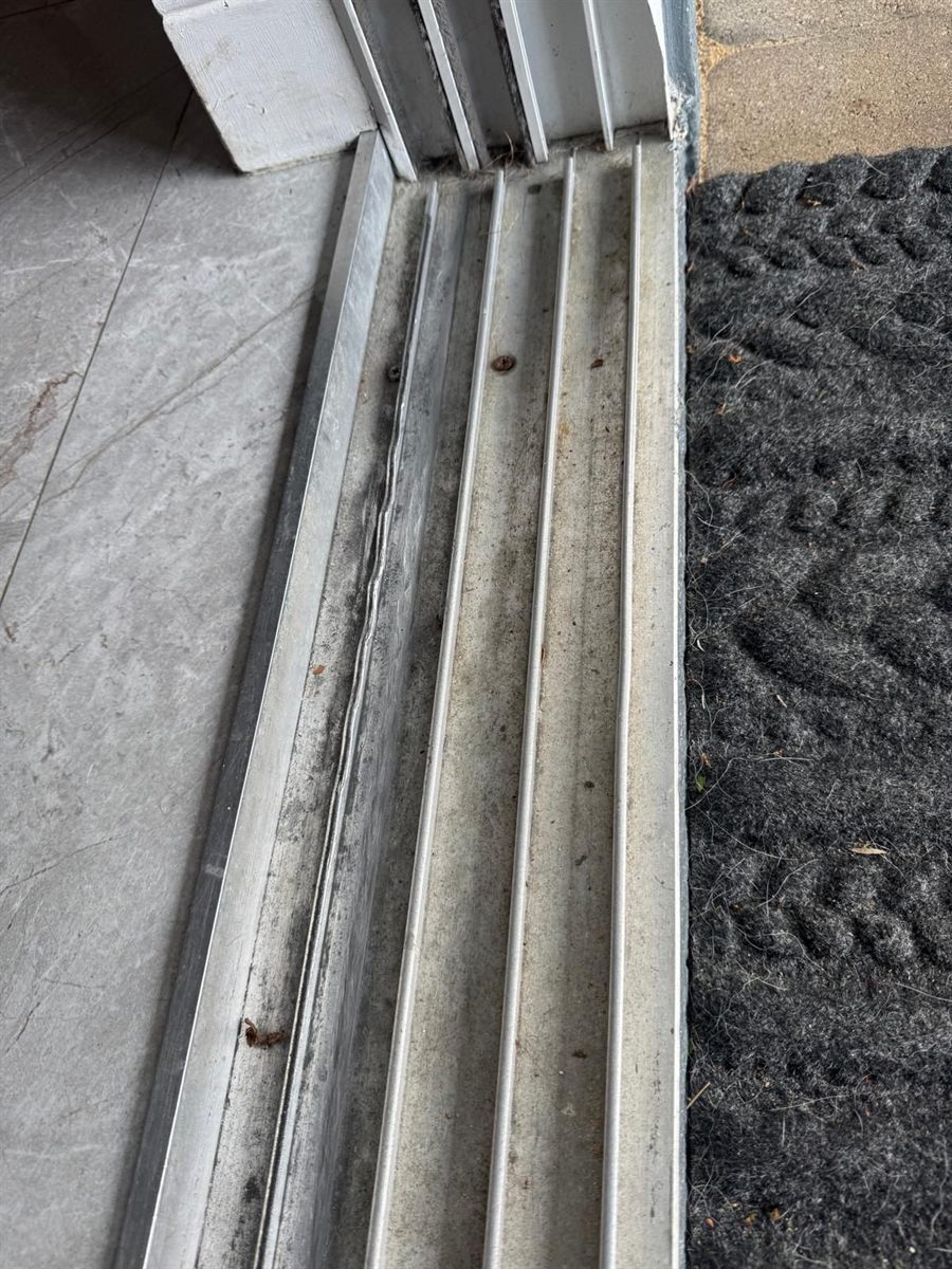 Real four-channel aluminum sliding-door bottom track at a Lake Mary home — marble tile floor on one side, doormat on the other, channels Speedy straightens, caps, or replaces