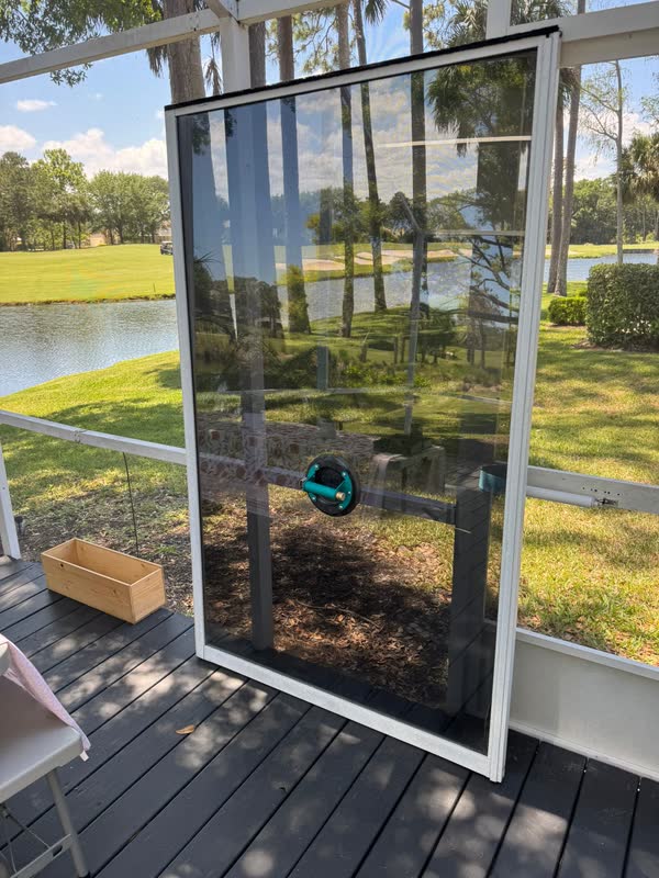 Sliding glass door panel removed and propped on a screened lanai overlooking a pond and golf course at a Central Florida home, vacuum suction handle attached