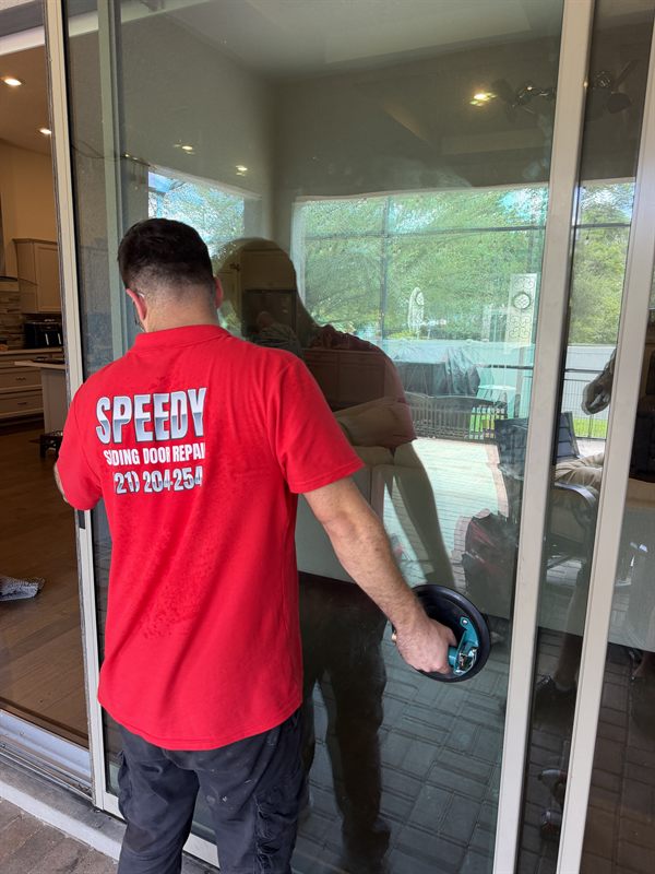 Speedy technician in a red SPEEDY Sliding Door Repair polo, seen from behind, using a blue vacuum suction handle on a large sliding glass door at a screened pool-lanai home in Central Florida