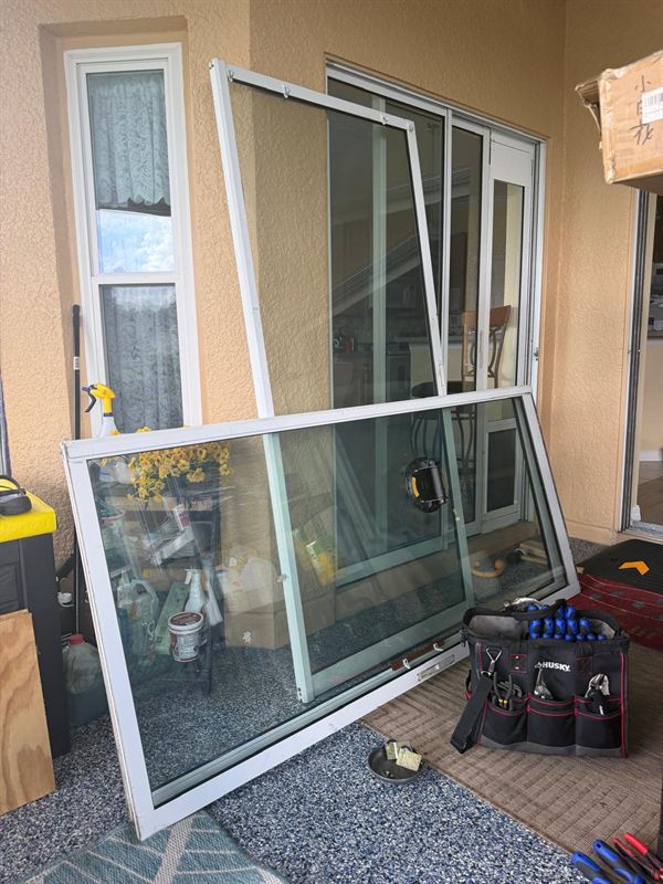 Two large sliding glass door panels removed and leaning on a screened lanai during a Speedy whole-house restoration, a vacuum suction handle on the glass and a Husky tool bag staged on the floor at a Central Florida pool home