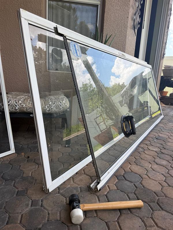 Large sliding glass door panel lifted out and leaning on a paver patio with a vacuum suction handle on the glass — Speedy Sliding Door Repair, Central Florida.
