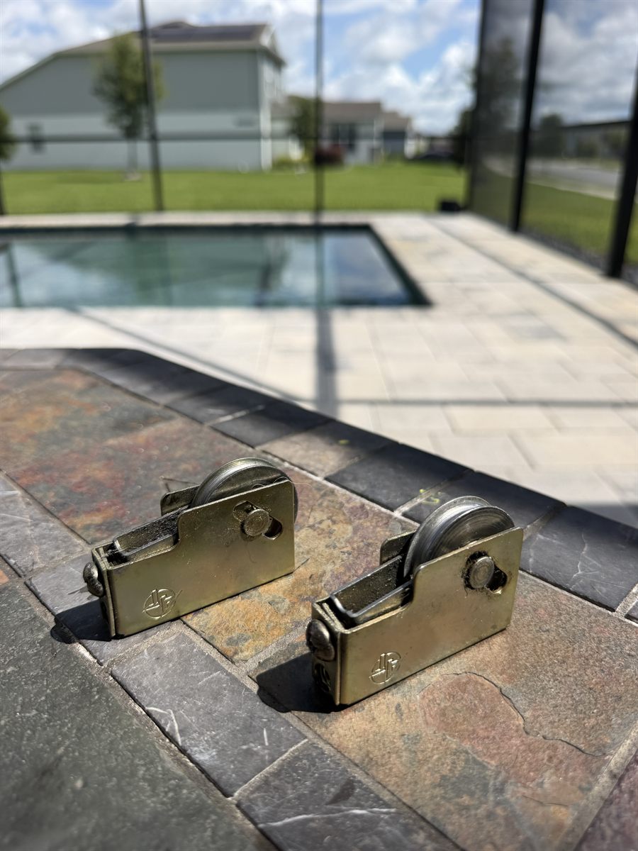 Two replacement stainless sliding door rollers ready to install at a Central Florida pool-lanai home — Speedy Sliding Door Repair, Gotha FL
