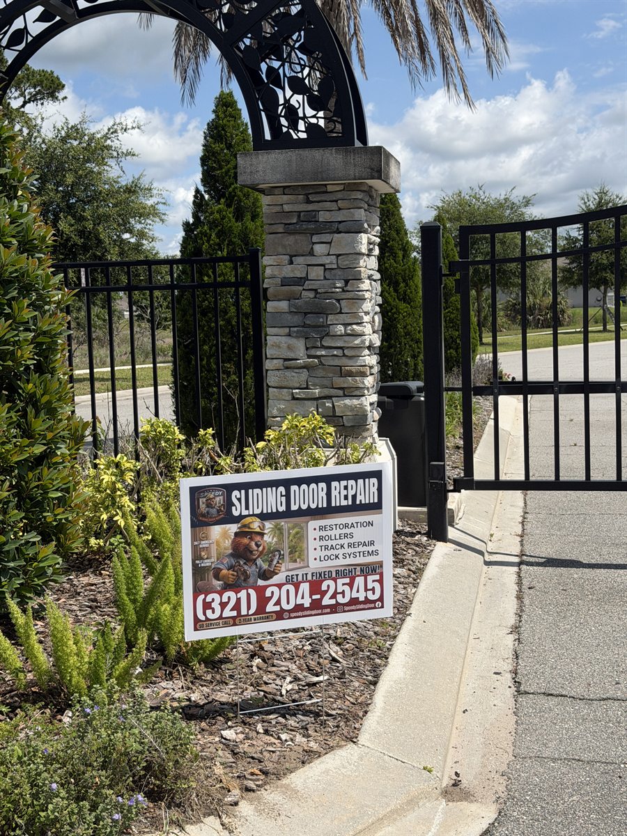 Speedy Sliding Door Repair yard sign planted at a gated Central Florida community entrance — stone columns, palm tree, sidewalk