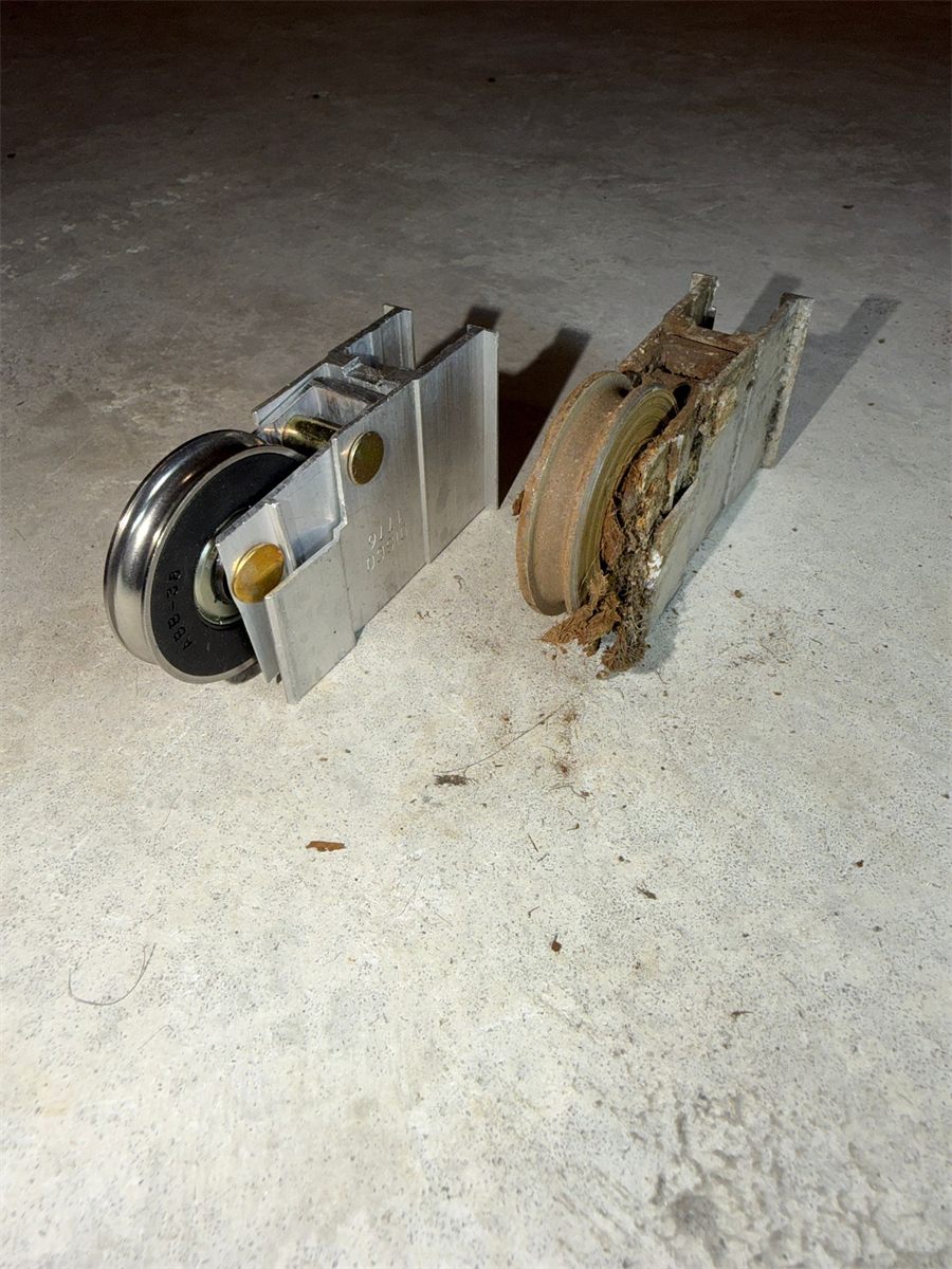 Real before-and-after: a worn rusty sliding door roller next to a brand new chrome stainless-steel replacement